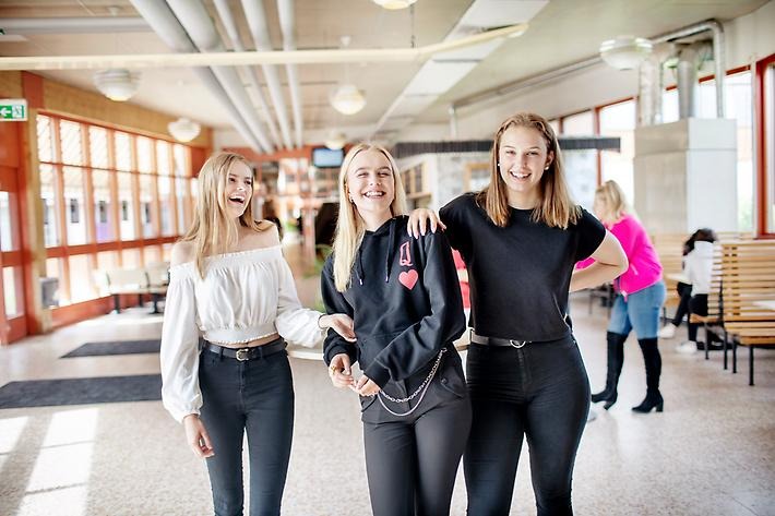 Tre glada tjejer i en skolkorridor